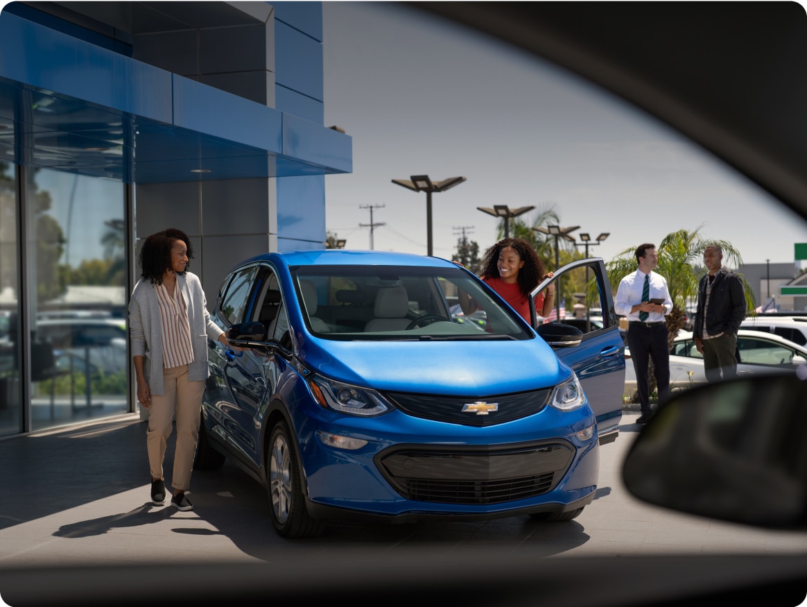 Two Women Smiling and Getting into a New Chevy Bolt EV from a Dealership's Lot
