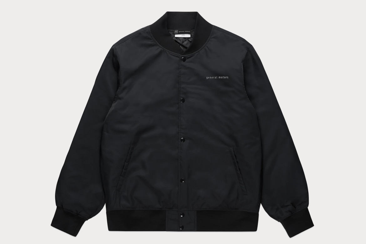 Black Collegiate Bomber Jacket With General Motors Text on Chest. It Has Button-Up Front, Side Pickets, and Ribbed Cuffs