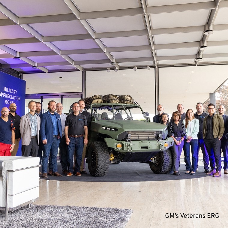 A Group Picture of a GM Veterans Employee Resource Group Smiling and Standing Next to an Old Military Vehicle