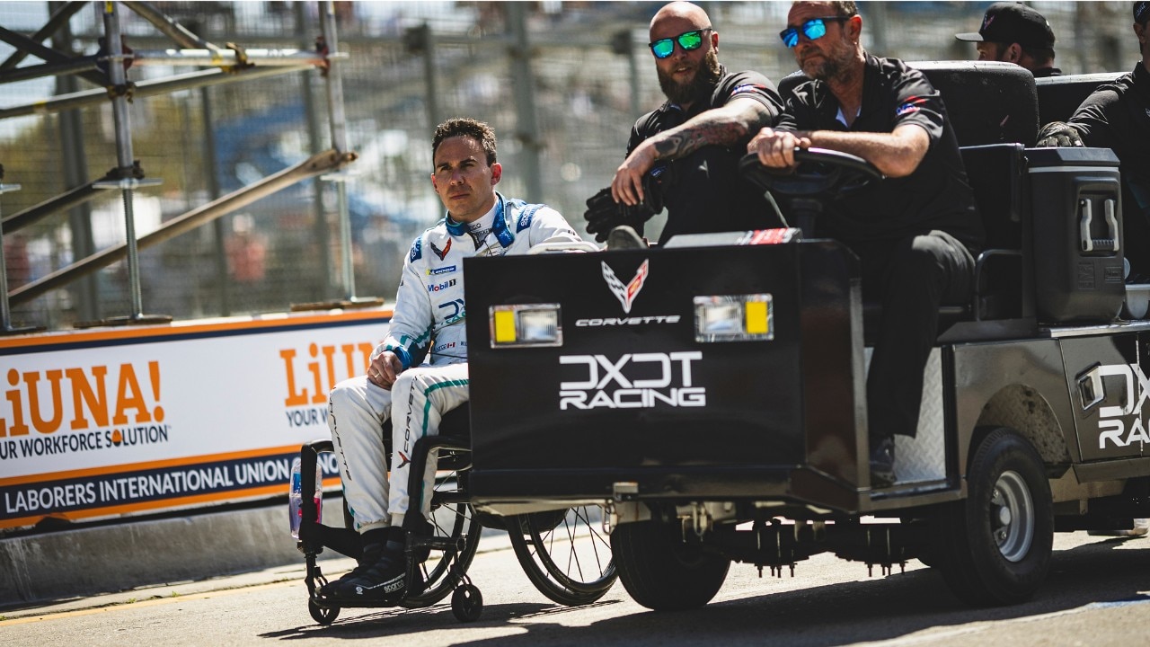 Close-up of Pro Race Car Driver in a Wheelchair on a Track Next to a Behind-the-scenes Cart