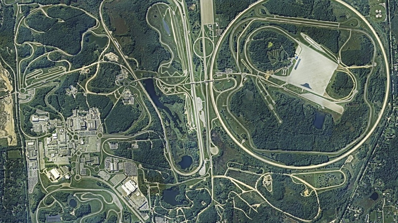 Aerial view of GM’s Milford Proving Ground, displaying high-speed test tracks and facilities in a forested landscape.