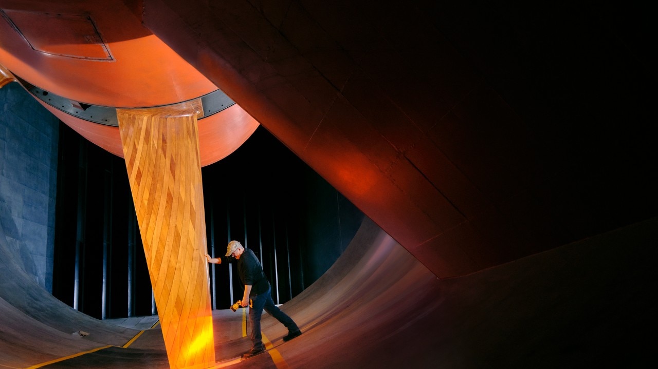 Engineer inspecting an orange vertical test panel inside a large automotive wind tunnel