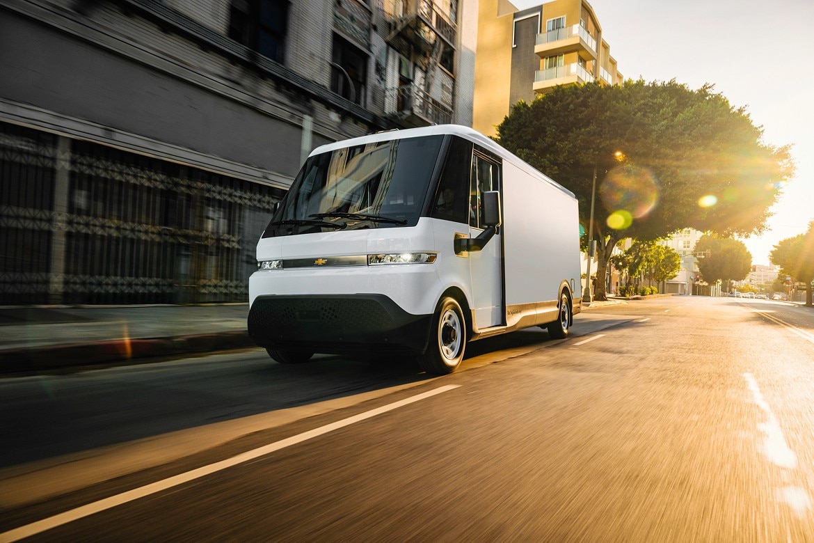 The all-electric BrightDrop Zevo 600 delivery van, branded with a Chevrolet badge, drives through a sunlit urban street.