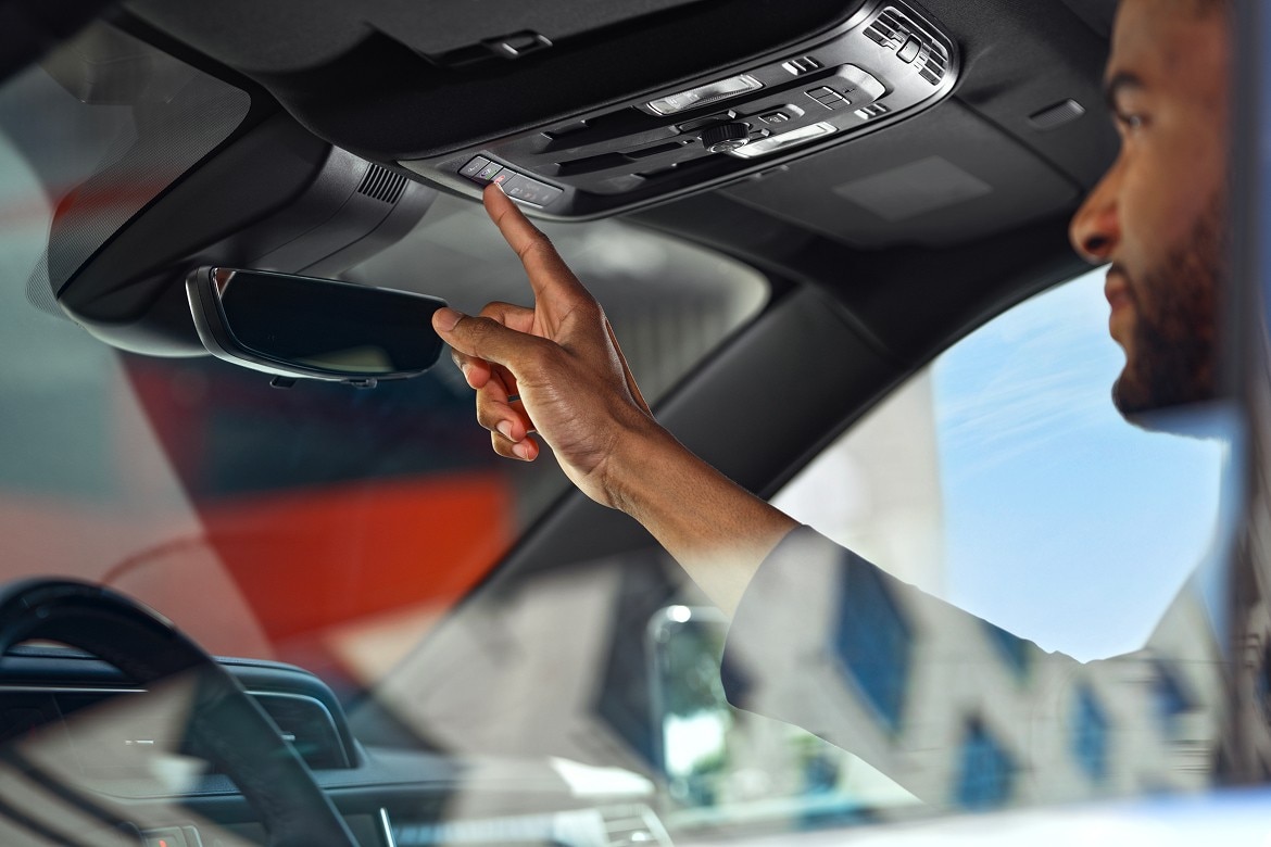 Driver inside a modern vehicle reaches up to press an overhead OnStar button near the rearview mirror.